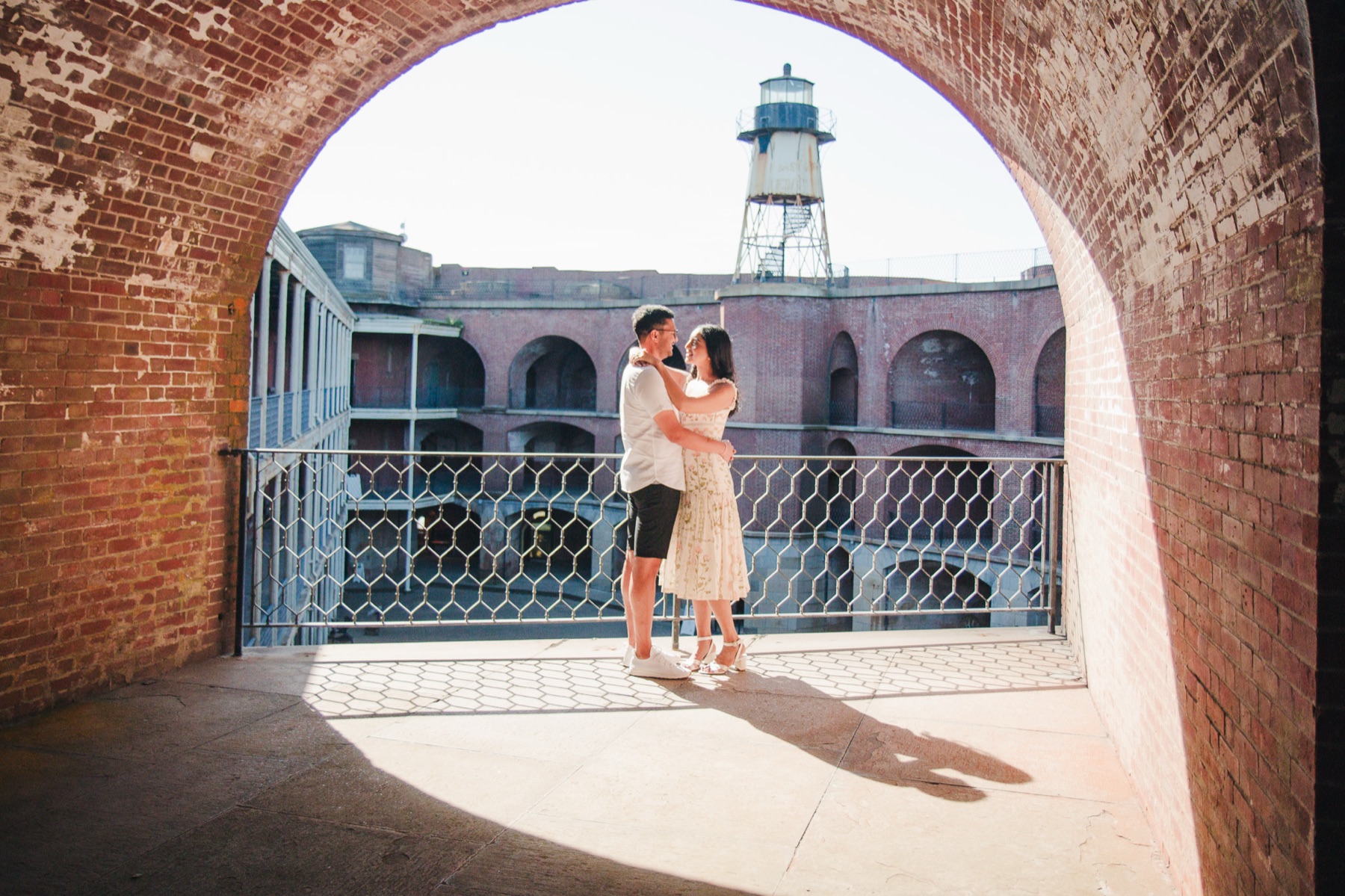 Ayushi and Aakash embracing inside a brick archway at Fort Point with the Golden Gate Bridge visible above