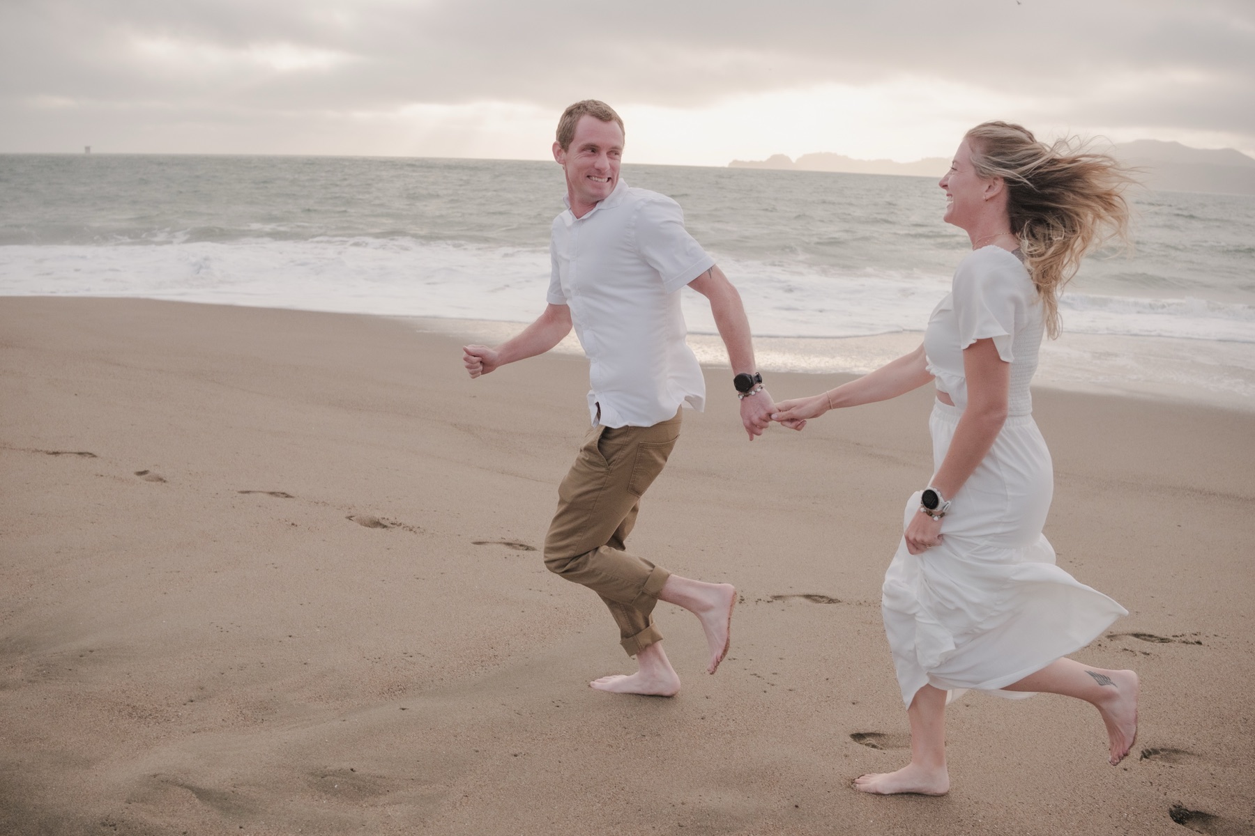 Maria and Jordan running hand in hand at Baker Beach, San Francisco engagement session